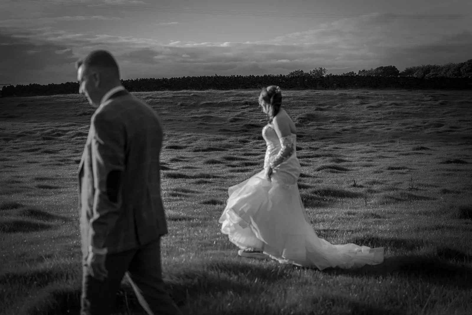 Black and white photo of a bride and groom walking through a field at dusk at a Lancashire wedding