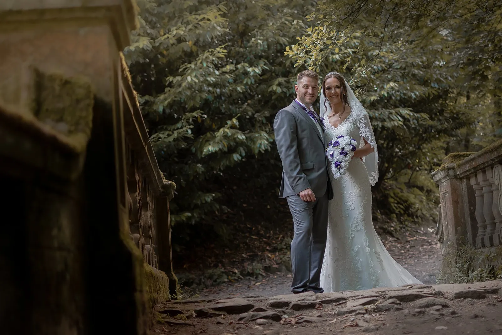 Bride and groom on a stone bridge over a brook, a water's-edge frame like the woodland ceremony area