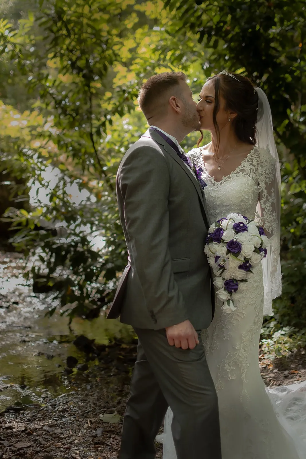 First kiss as husband and wife in front of green foliage, the bride still holding a white and eucalyptus bouquet