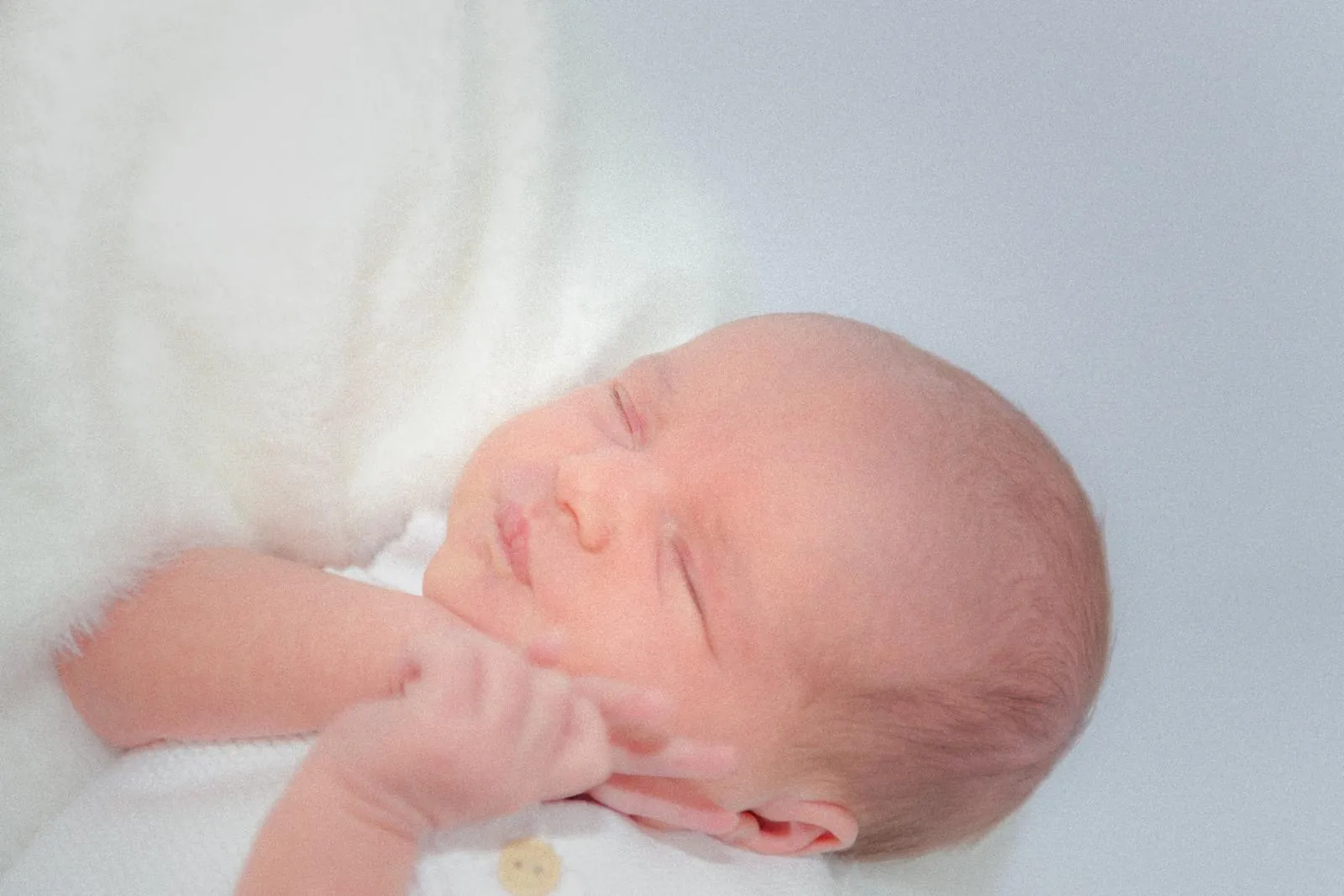 Newborn baby asleep on a soft white blanket, photographed close in daylight at home